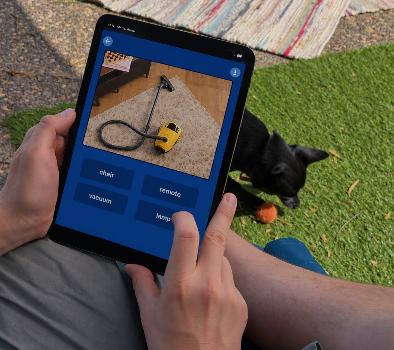 Hands on an iPad doing a Sanapsis+ word exercise outdoors, with a small black dog in the background