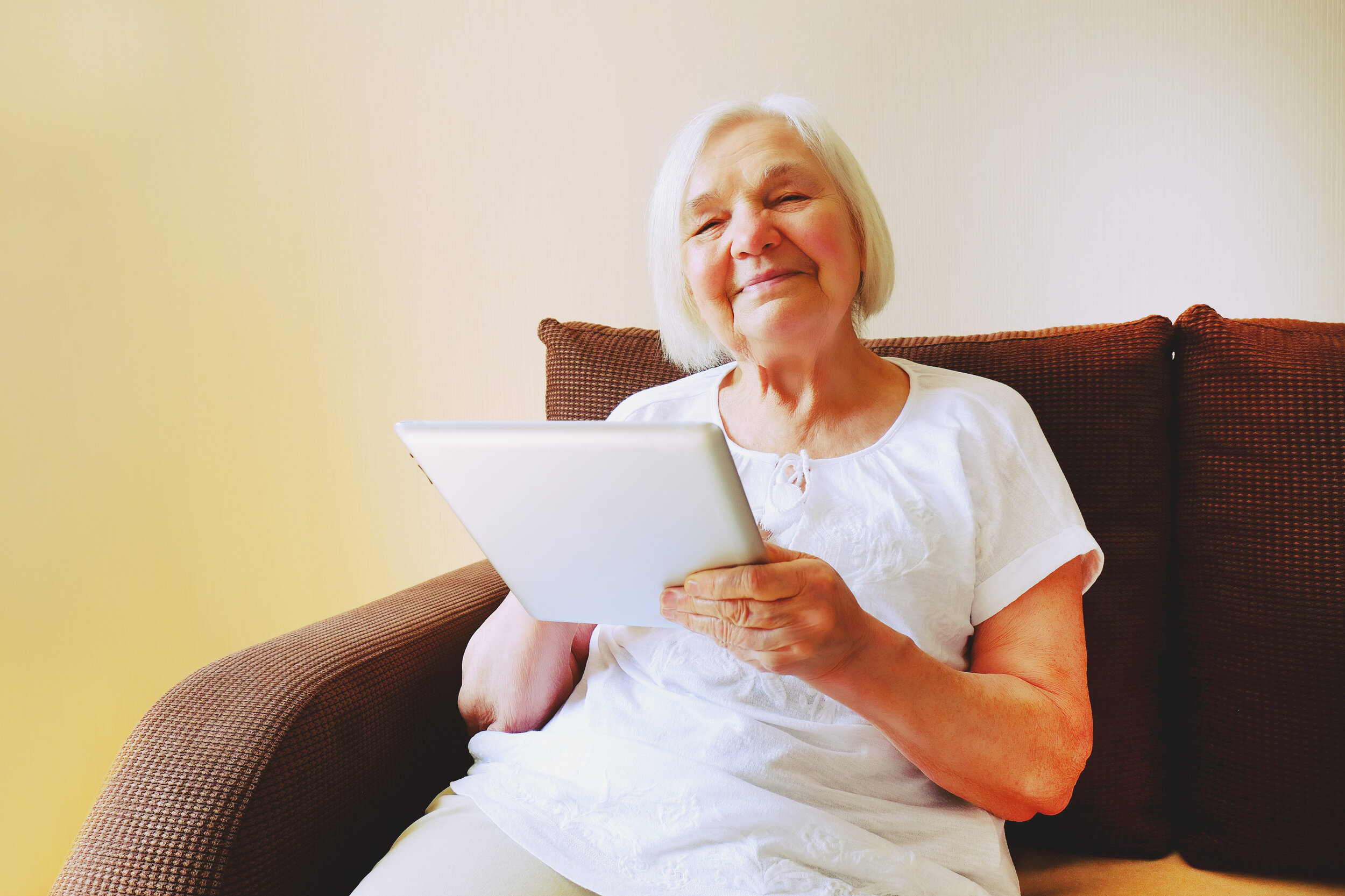 Smiling older woman on a sofa holding a tablet
